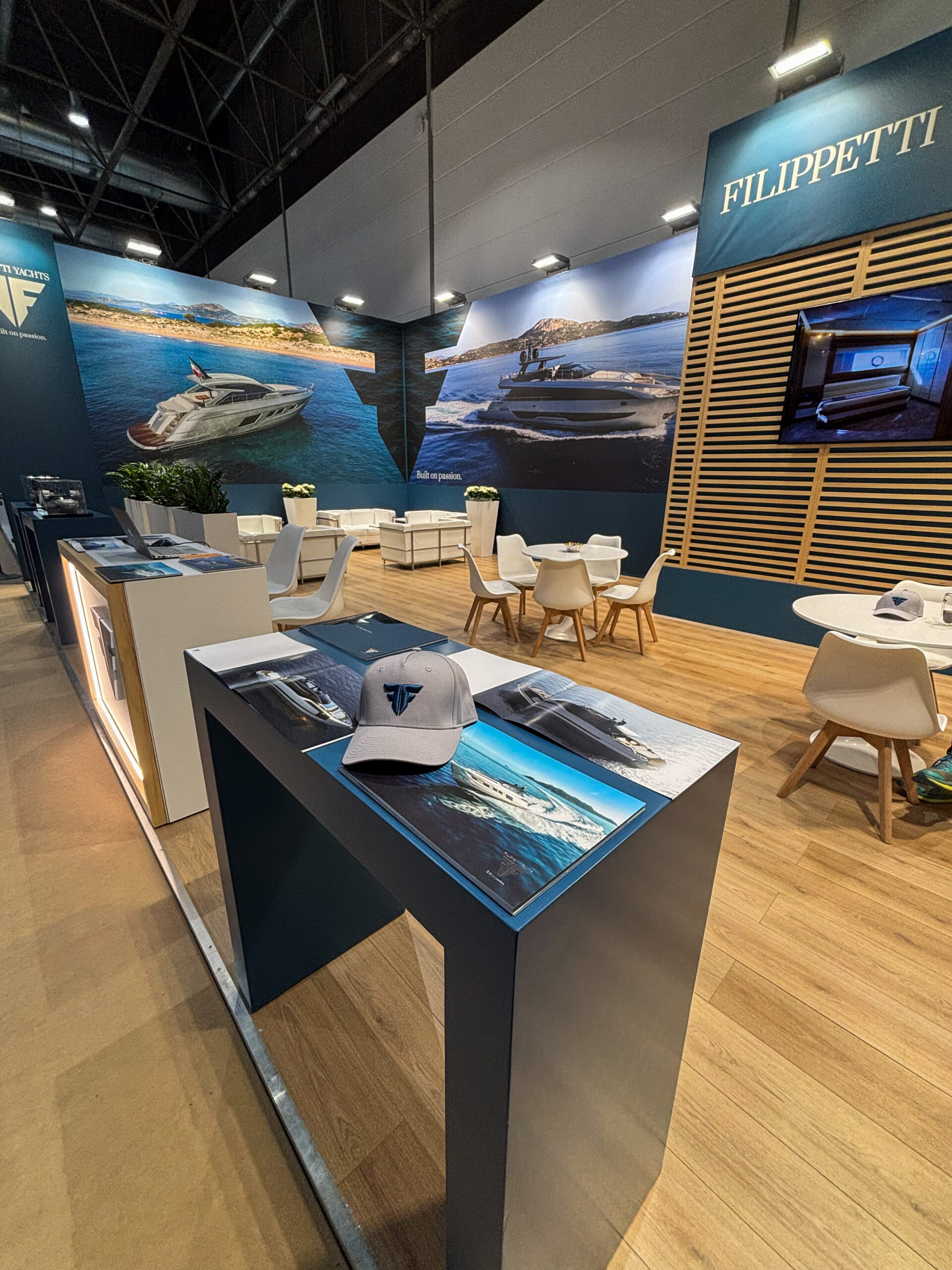 Filippetti Yachts exhibition stand featuring large screens with luxury motor yachts, an elegant lounge area, and branded merchandise.